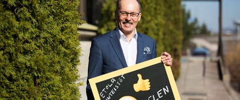 Etolan työntekijä pitää kylttiä, jossa hymynaama ja peukun kuva sekä tekstit Etola ja Helen